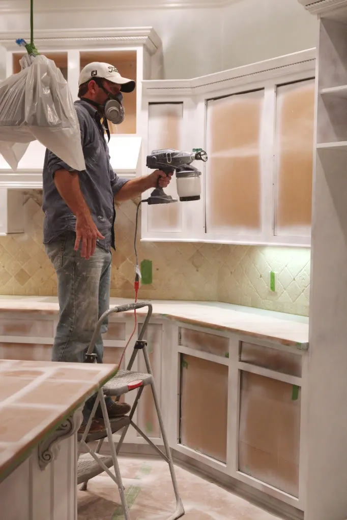 Professional kitchen cabinet refinishing in Ottawa - painter with spray equipment transforming white cabinets